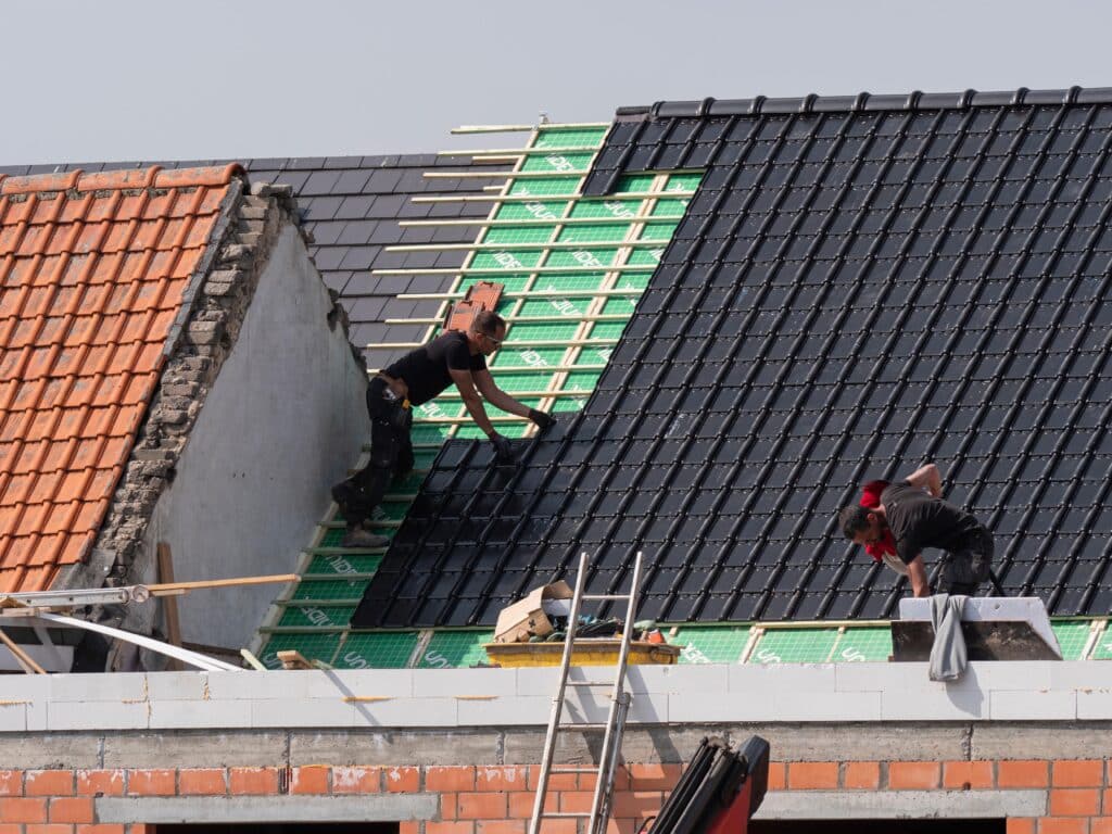 travaux de toiture réalisés par deux ouvriers en train de poser de nouvelles tuiles noires sur le toit d'une maison bruxelleoise