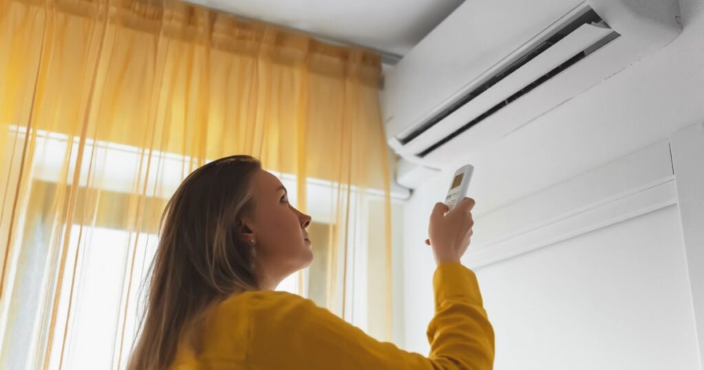 femme en train d'allumer le climatiseur monobloc de sa chambre pour ajuster la température de la pièce