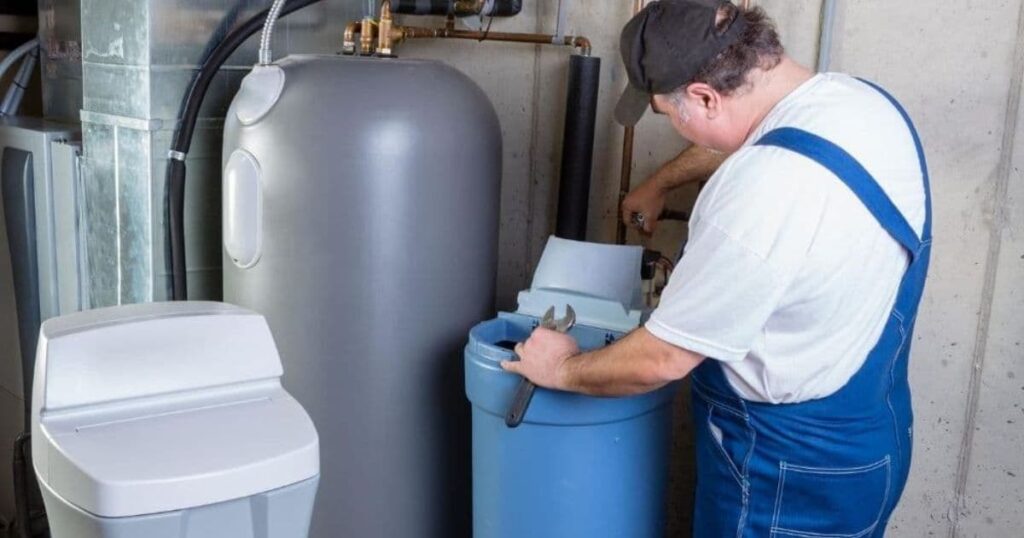 Plombier qui installe un adoucisseur d'eau avec une clé à molette à la main