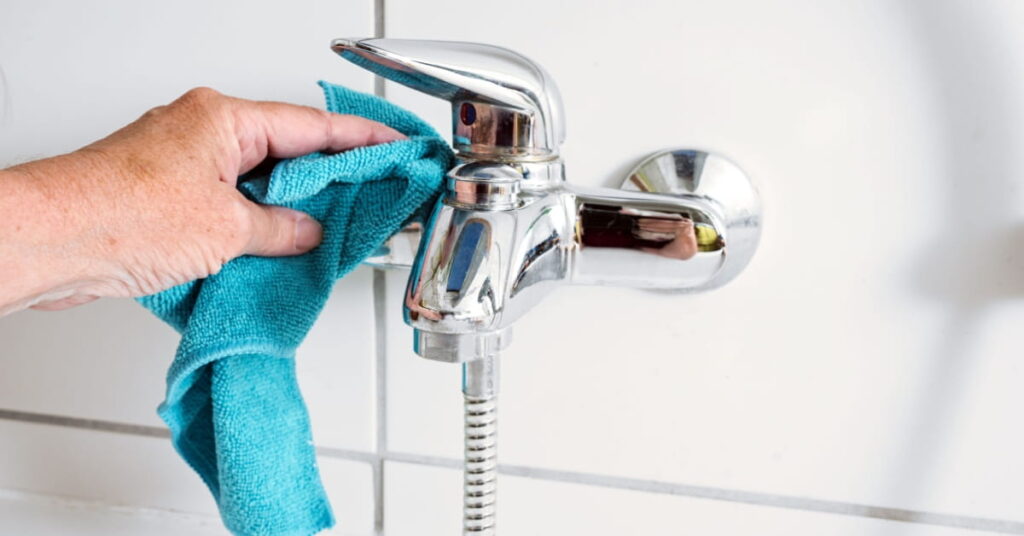 Personne nettoyant un robinet de douche à l'aide d'un chiffon
