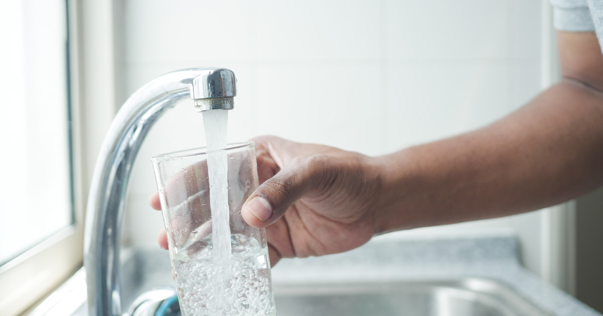 une main tendue vers un robinet pour remplir le verre d'eau