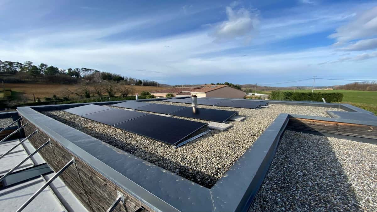 Des panneaux solaires Votec Solar sont installés sur une toiture plate. On voit d'autres habitations en arrière-plan ainsi qu'un ciel bleu nuageux.