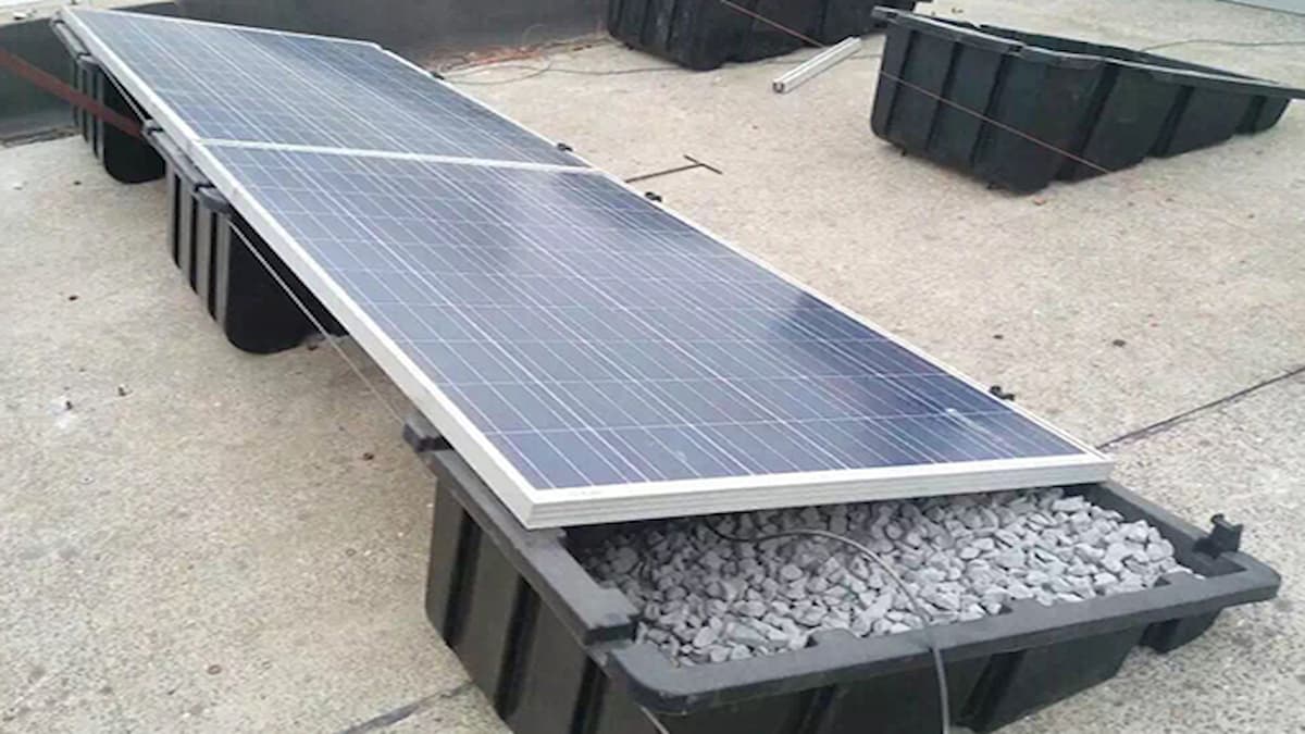 Un bac lesté de gravier sous un panneau solaire installé sur un sol gris.